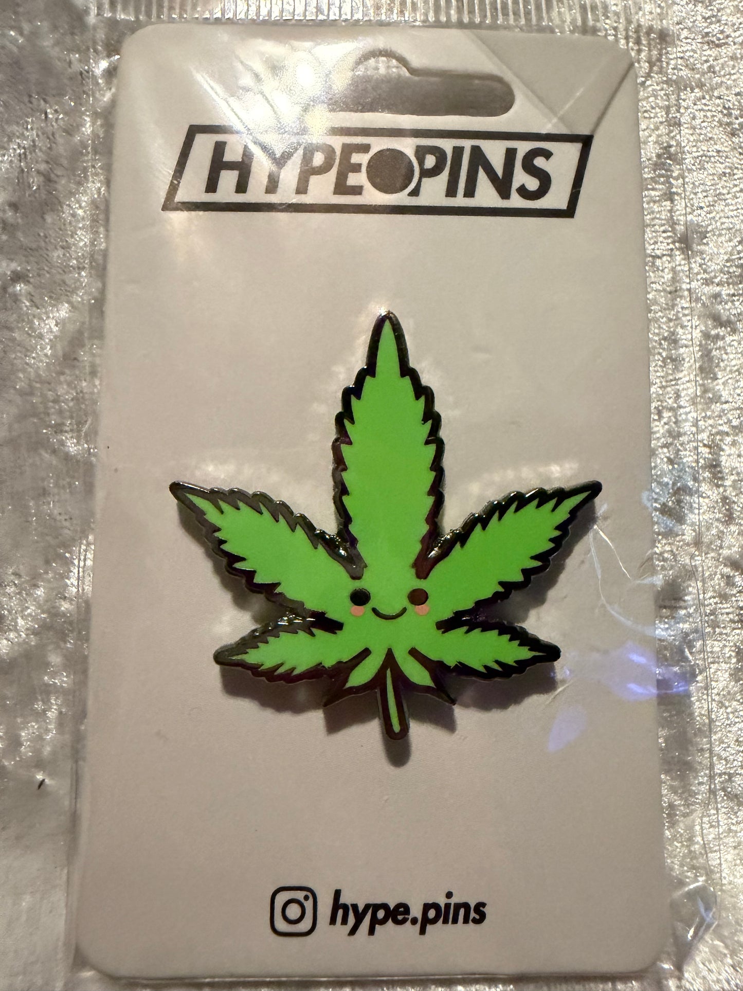 A 'Cute Weed Leaf' hard enamel pin from Hatcher's Collectibles, featuring a stylized green cannabis leaf design with a secure butterfly clutch backing