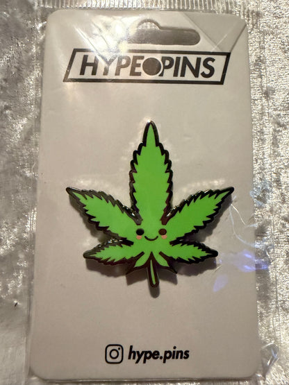 A 'Cute Weed Leaf' hard enamel pin from Hatcher's Collectibles, featuring a stylized green cannabis leaf design with a secure butterfly clutch backing