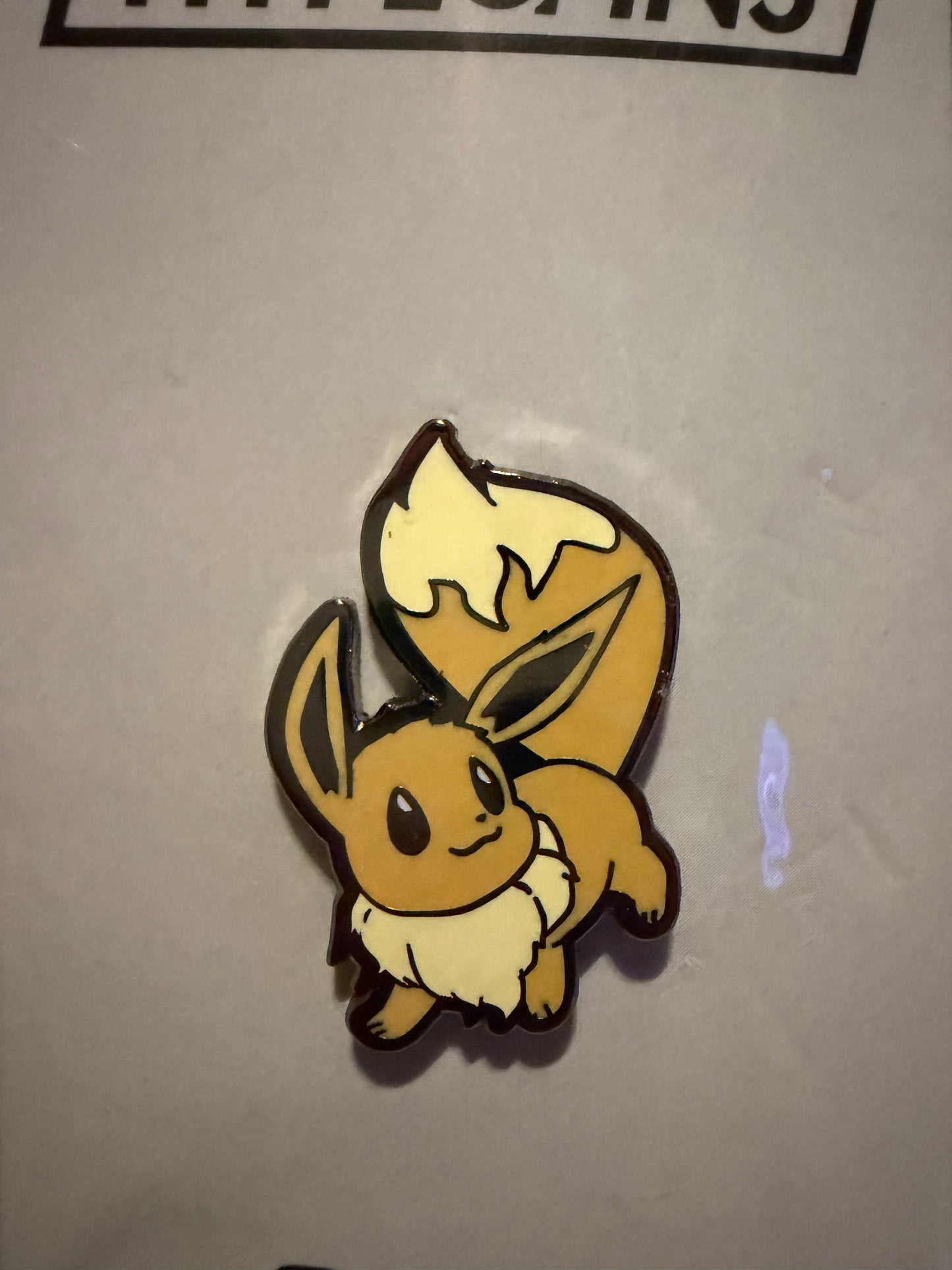 Close-up of the **Pokémon Eevee Hard Enamel Pin**, showcasing its adorable expression, vibrant colors, and sleek hard enamel finish. A detailed Eevee collectible by Hype Pins.