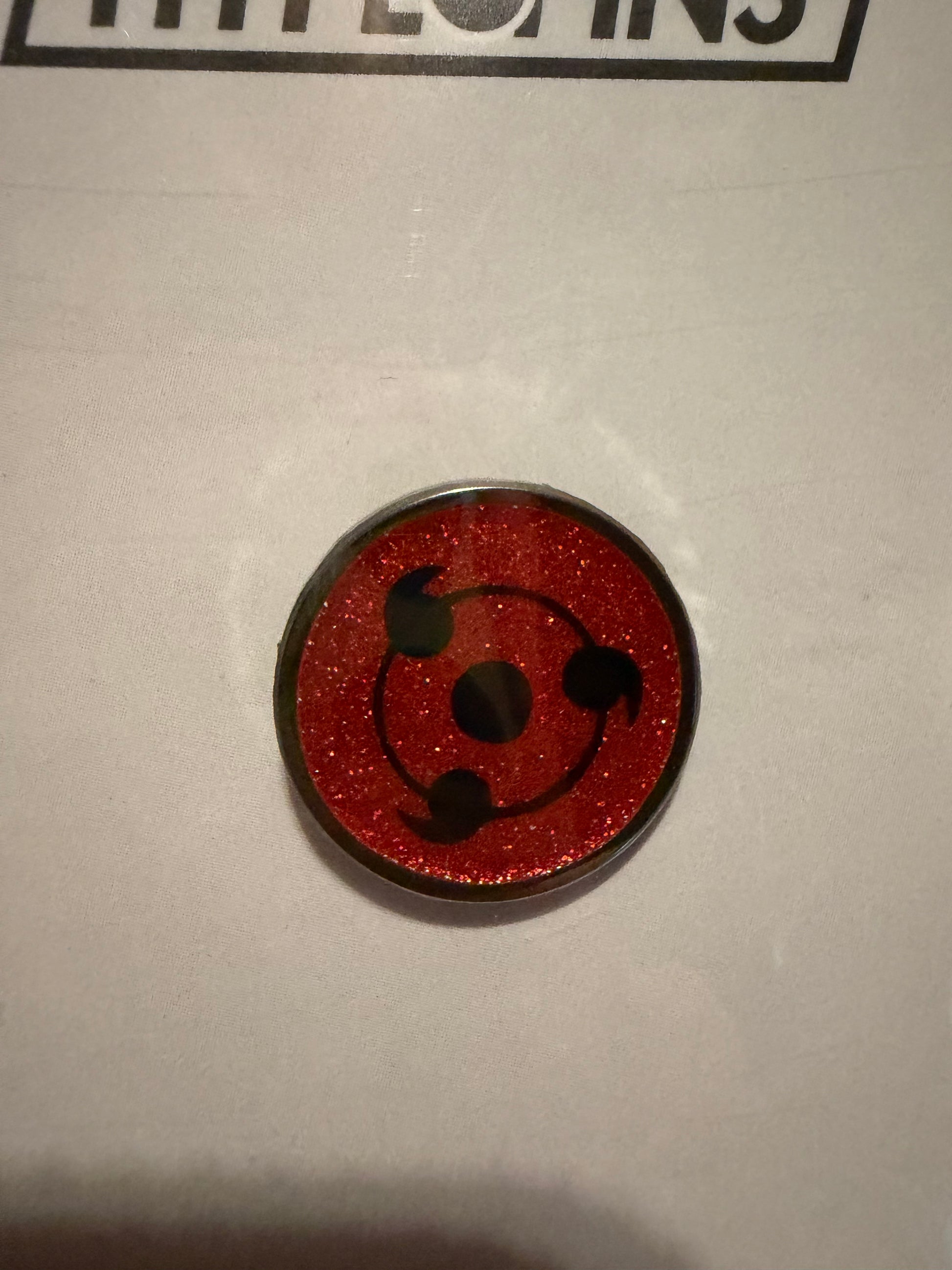 Close-up of the **Sharingan Obito Hard Enamel Pin**, highlighting the intricate details of the Mangekyo Sharingan, vibrant colors, and sleek hard enamel finish. A powerful Naruto anime collectible.