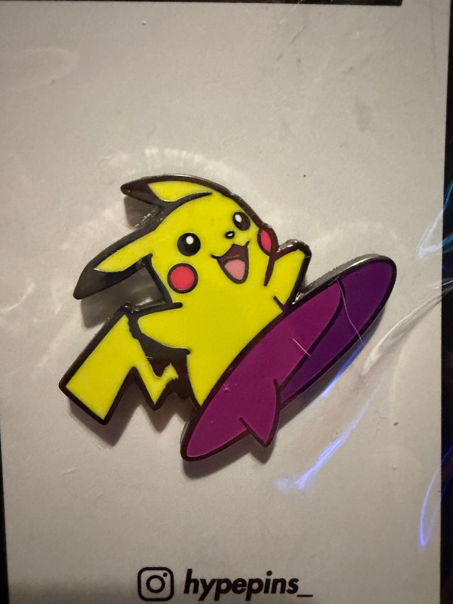 Close-up of the **Surfing Pikachu Hard Enamel Pin**, highlighting Pikachu riding a wave, vibrant colors, and sleek hard enamel finish. A detailed Pokémon collectible by Hype Pins.