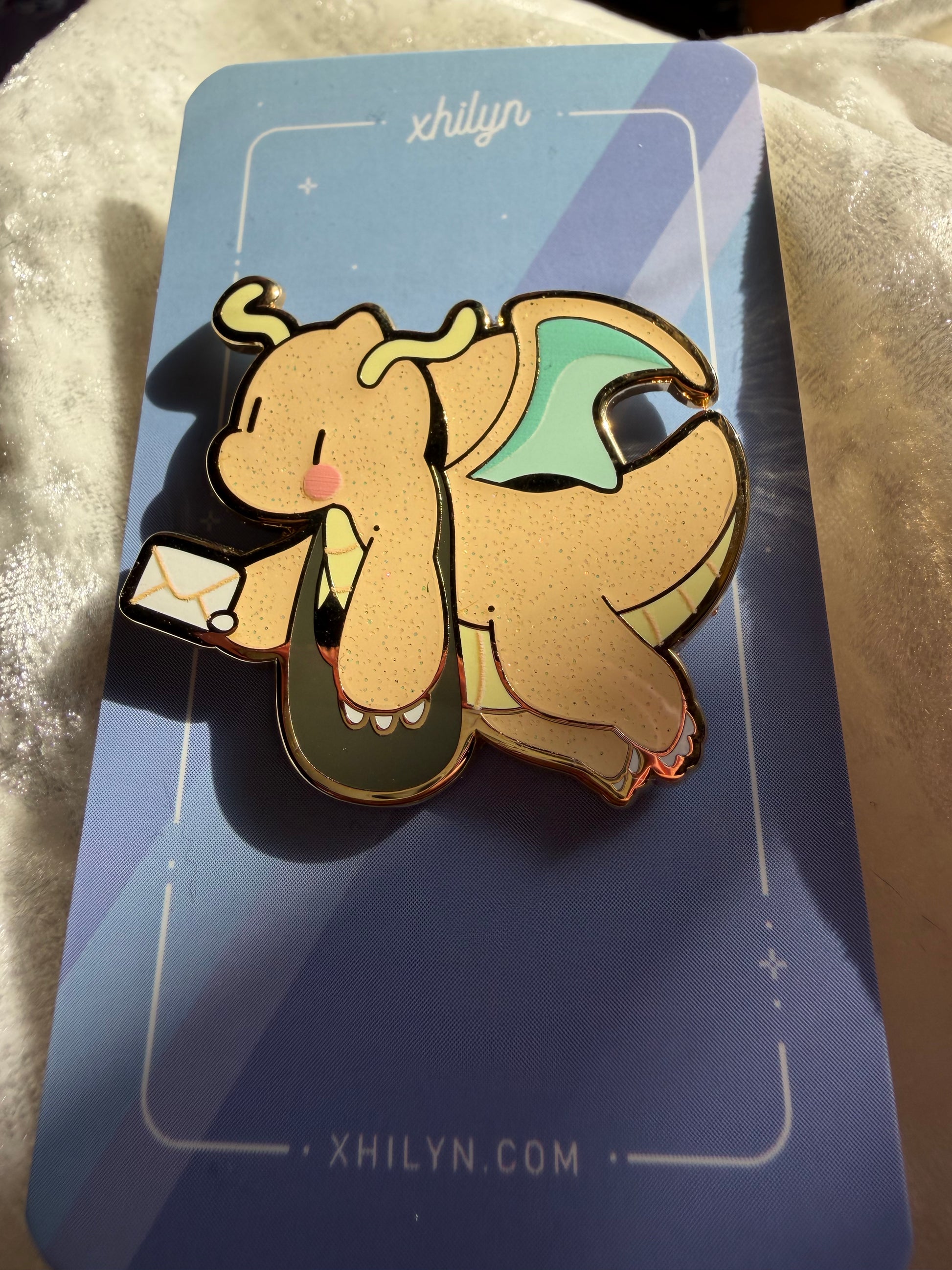 Delivery Dragonite enamel pin by Xhilyn, with gold metal, glitter, and UV print, featuring a cheerful Dragonite holding an invitation from Hatcher’s Collectibles