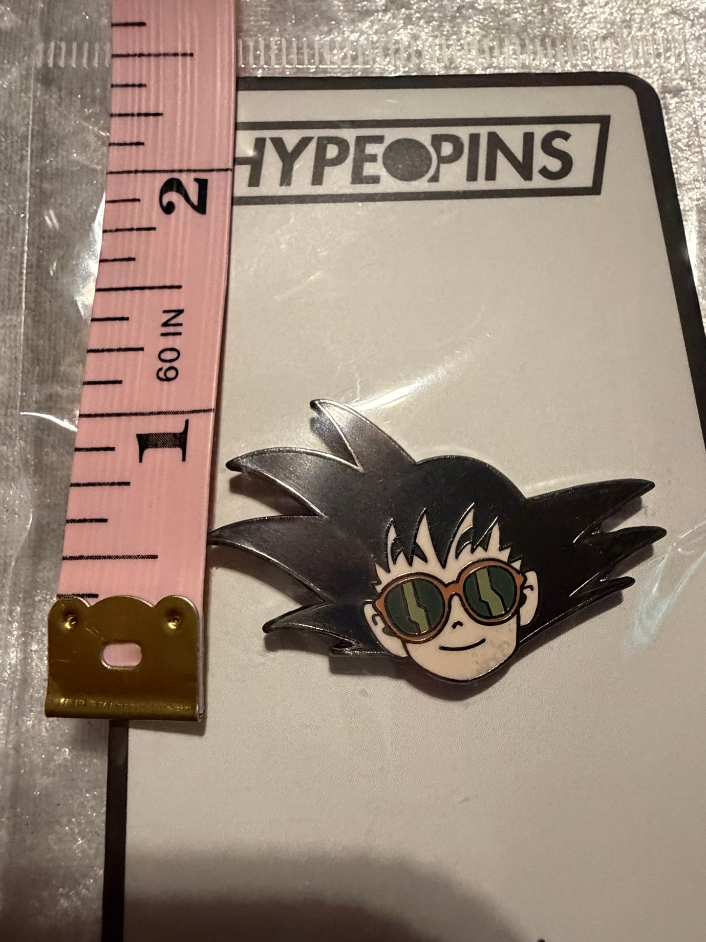 Goku Chillin Dragon Ball Z Enamel Pin next to a tape measure, clearly displaying its 1.5-inch size, highlighting its perfect collectible scale.