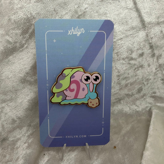 Gold metal Gary sea snail enamel pin pinned to a colorful blue card 