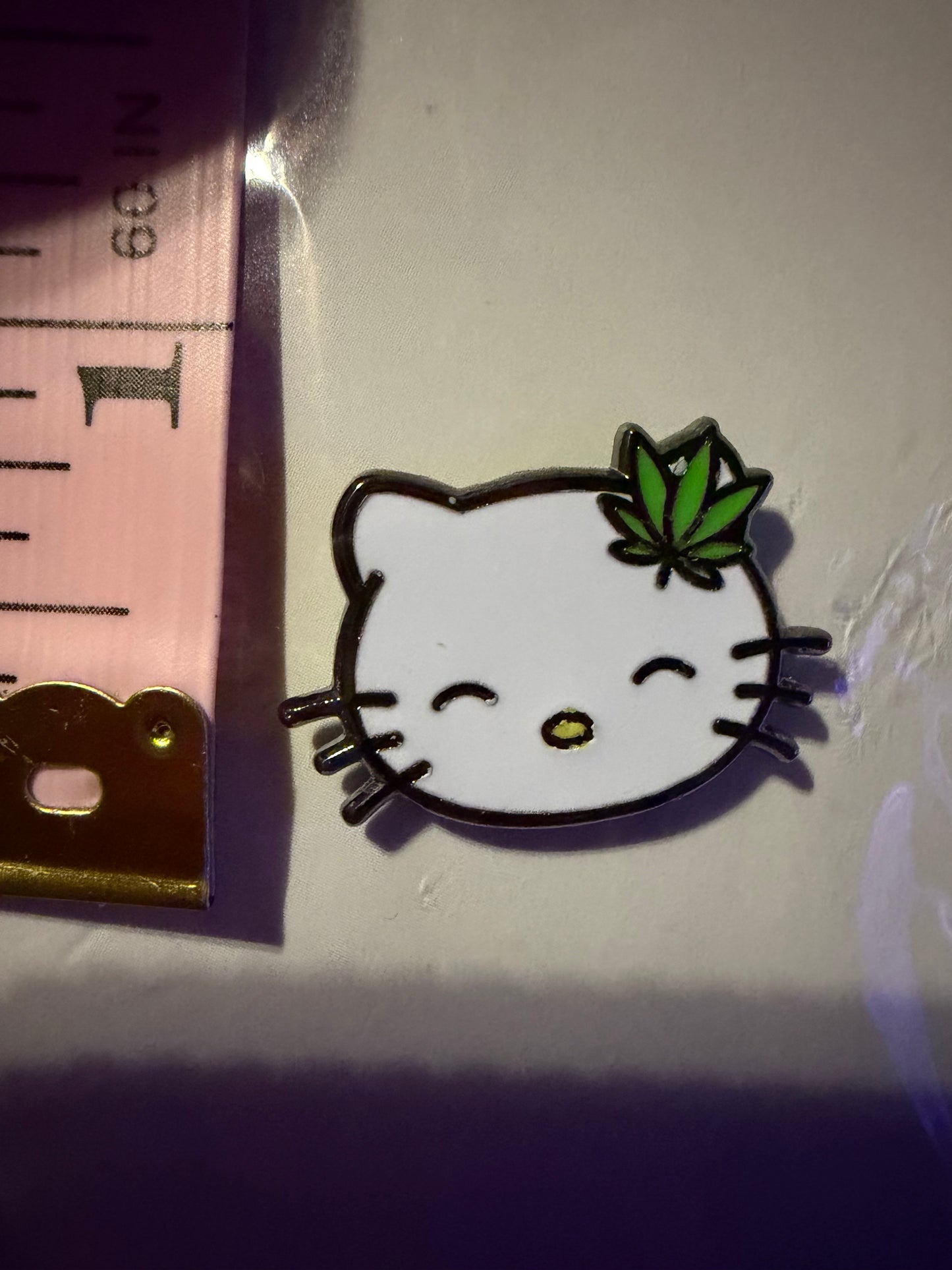 Hello Litty Hard Enamel Pin next to a tape measure, clearly displaying its **1.25-inch size** and quality craftsmanship. Perfect for your pop culture collection.
