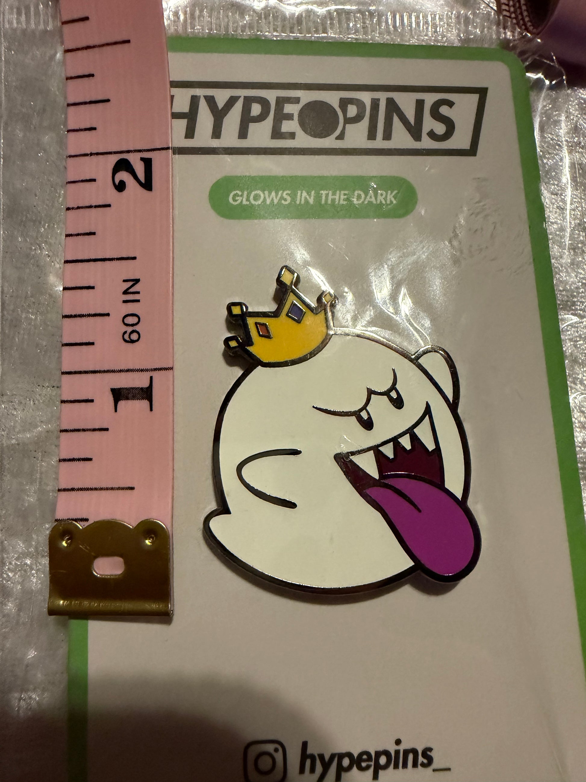 King Boo Glow In The Dark Enamel Pin by Hype Pins, shown next to a tape measure to demonstrate its **1.5-inch size**. This Super Mario collectible **glows in the dark**.