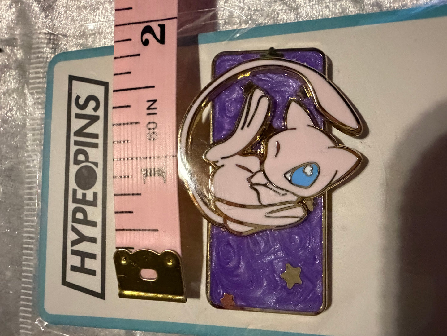 Mew Galaxy Spinning Pokémon Enamel Pin by Hype Pins, positioned next to a tape measure to illustrate its **1.75-inch size**. Highlights its gold plating and spinning feature.