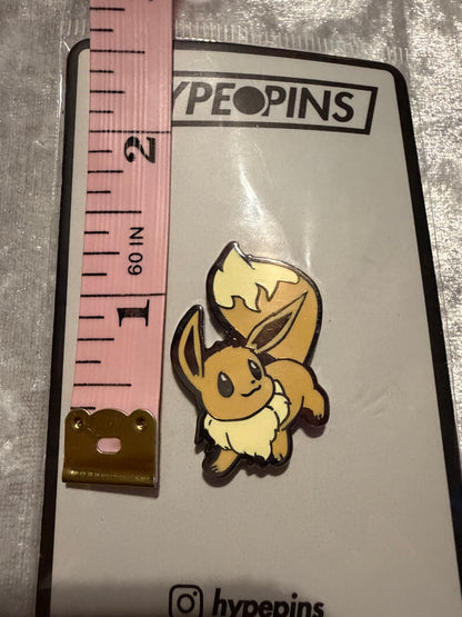 Pokémon Eevee Hard Enamel Pin by Hype Pins, displayed next to a tape measure to show its **1.25-inch size**. This cute Eevee collectible features a durable hard enamel and black nickel metal finish.