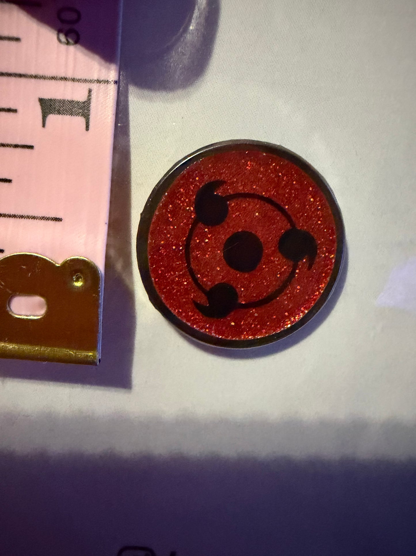 Sharingan Obito Hard Enamel Pin by Hype Pins, displayed next to a tape measure to show its **.75-inch size**. This Naruto anime collectible features a durable hard enamel and black nickel metal finish.