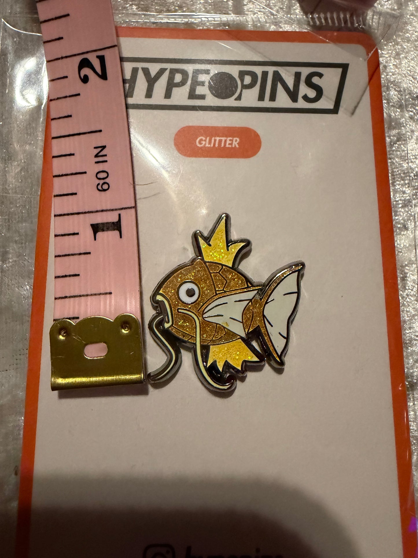 Shiny Magikarp Hard Enamel Pin by Hype Pins, shown next to a tape measure to illustrate its **1-inch size**. This rare Pokémon collectible features its iconic golden scales.