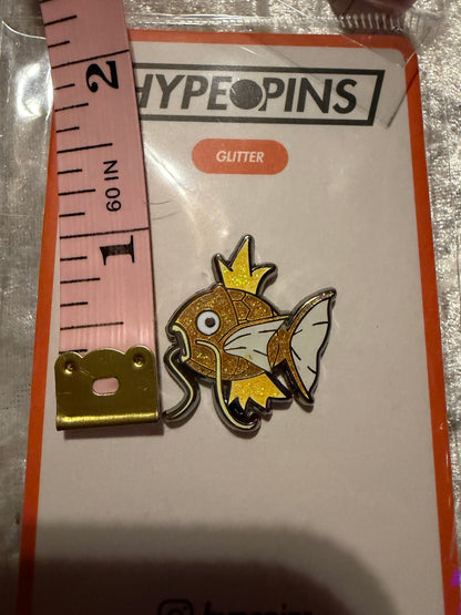 Shiny Magikarp Hard Enamel Pin by Hype Pins, shown next to a tape measure to illustrate its **1-inch size**. This rare Pokémon collectible features its iconic golden scales.