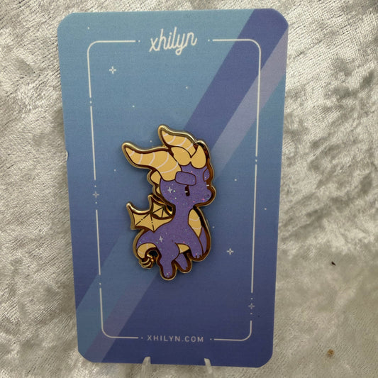 Spyro the Dragon enamel pin with purple and yellow rainbow glitter displayed on a custom Xhilyn backing card.