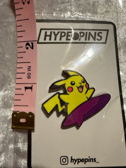 Surfing Pikachu Hard Enamel Pin by Hype Pins, displayed next to a tape measure to show its **1.5-inch size**. This dynamic Pokémon collectible features a durable hard enamel and black nickel metal finish.